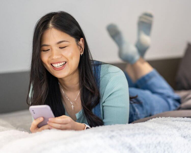 image of a student lying on a bed looking at her phone